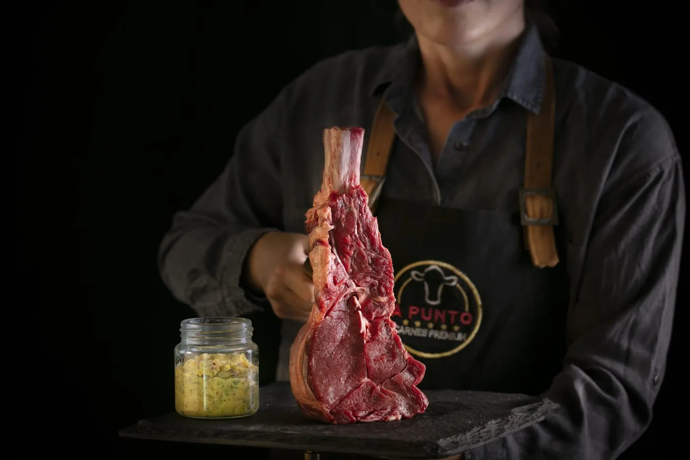 Carnicero A Punto con delantal de cuero sosteniendo un tomahawk crudo