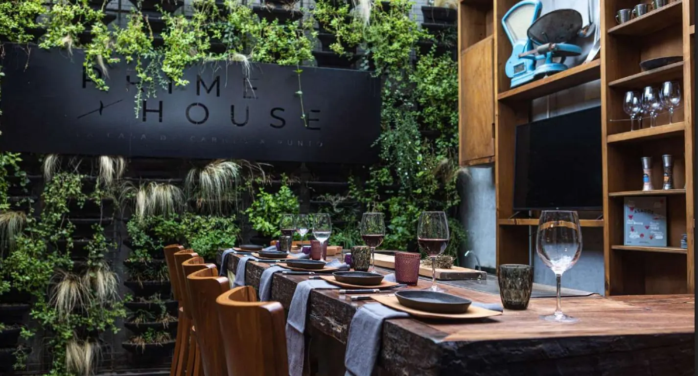 Mesa larga puesta en el quincho del Prime House, con muro verde y el letrero iluminado